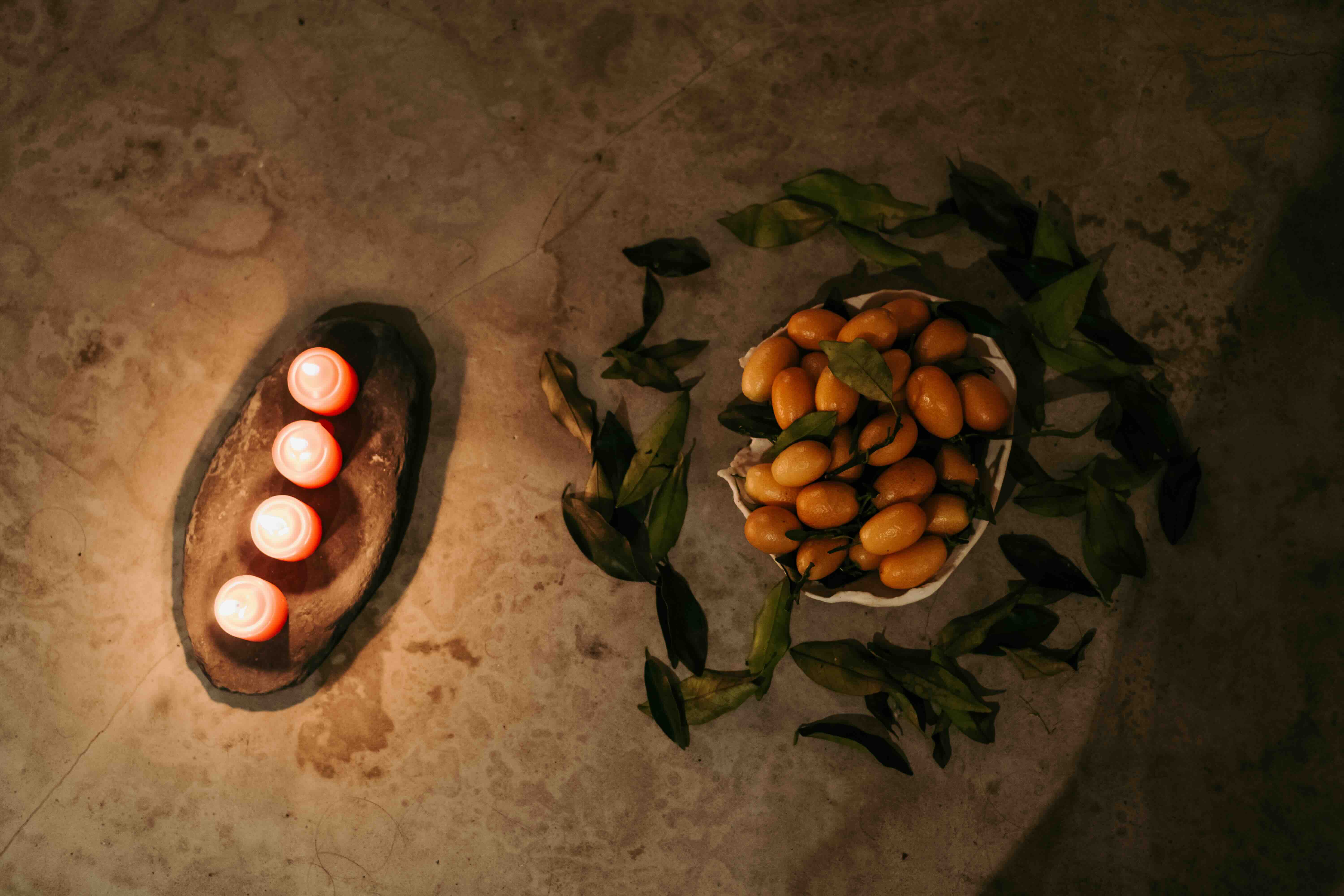 Candles in a stone bowl beside a bowl of fruit and leaves, laid out for a ritual