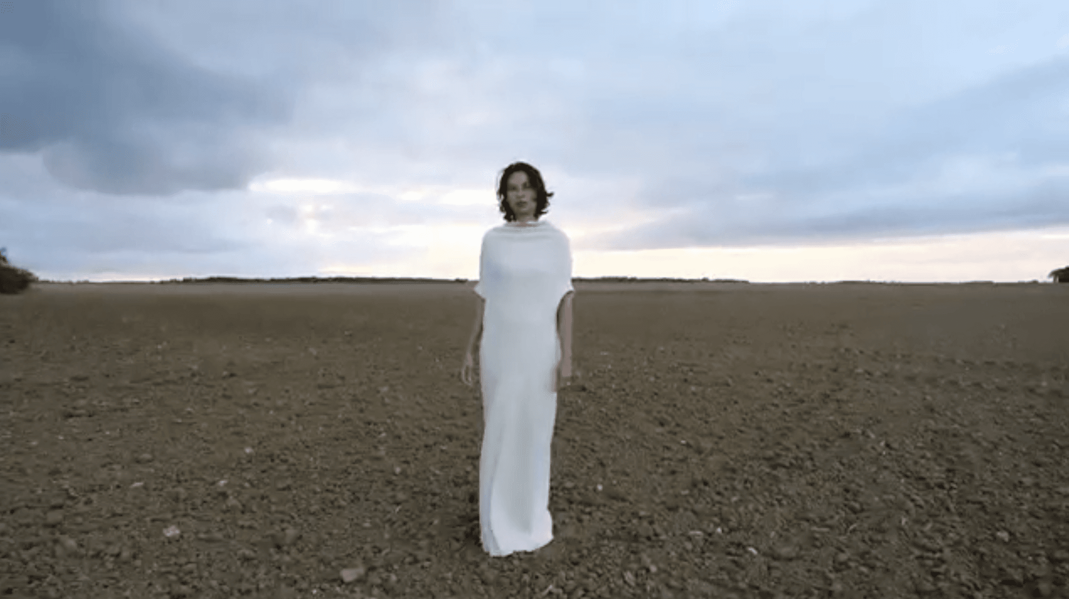 Sylvie Barbier in a long white dress in a ploughed field
