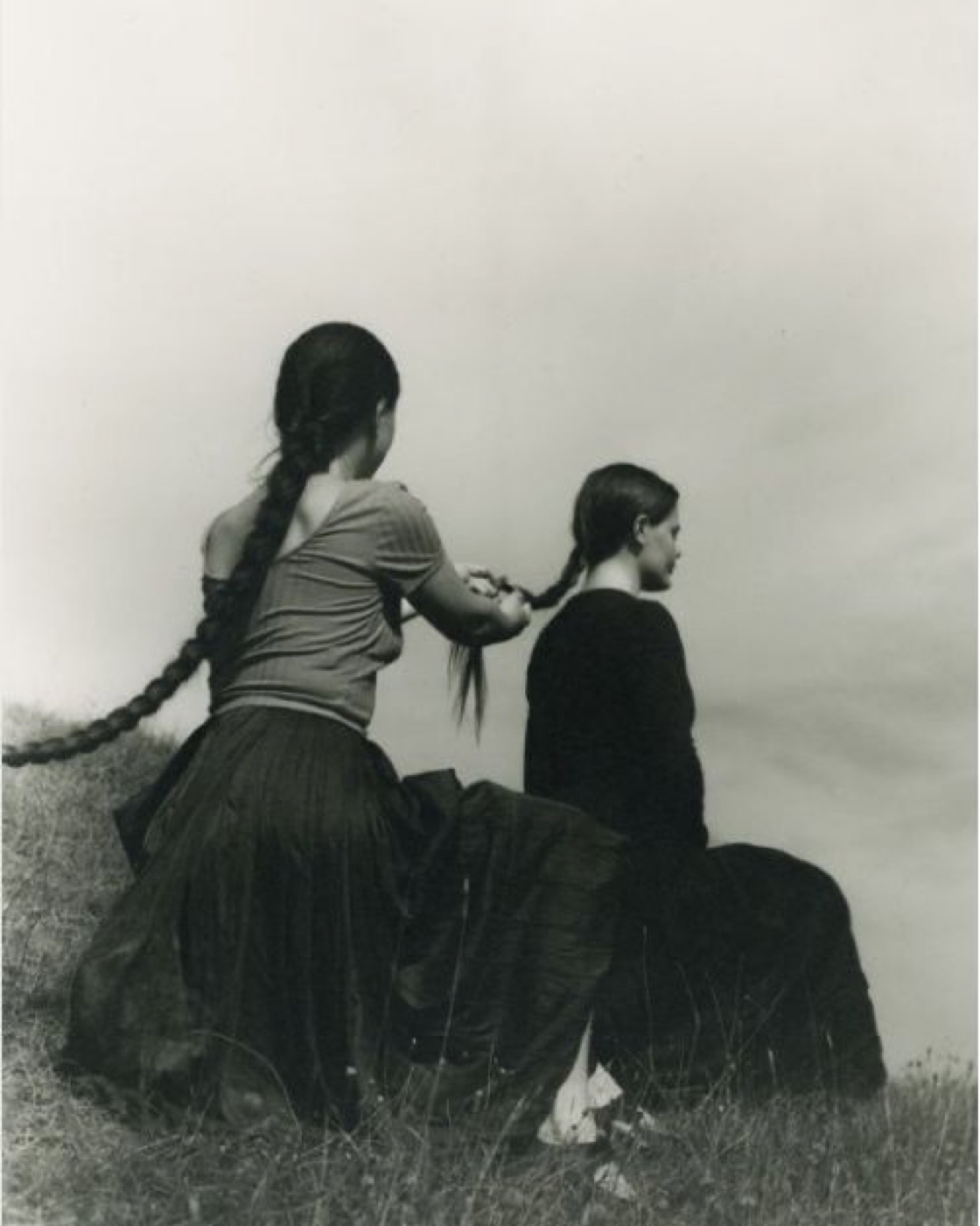 Two women on a grassy hill, one braiding the other's hair