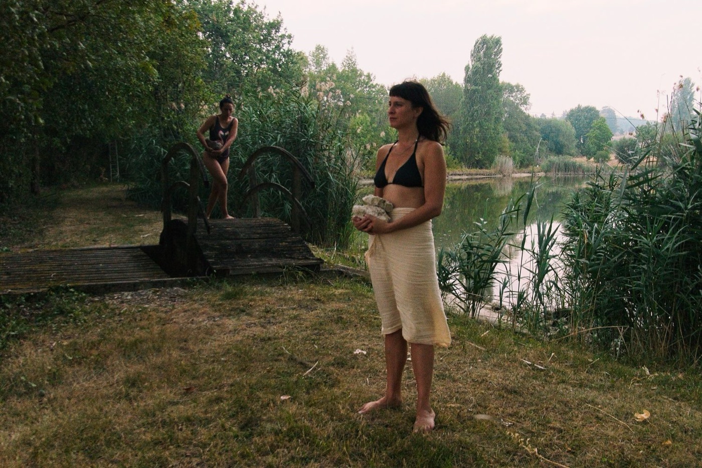A woman holds stones beside a lake